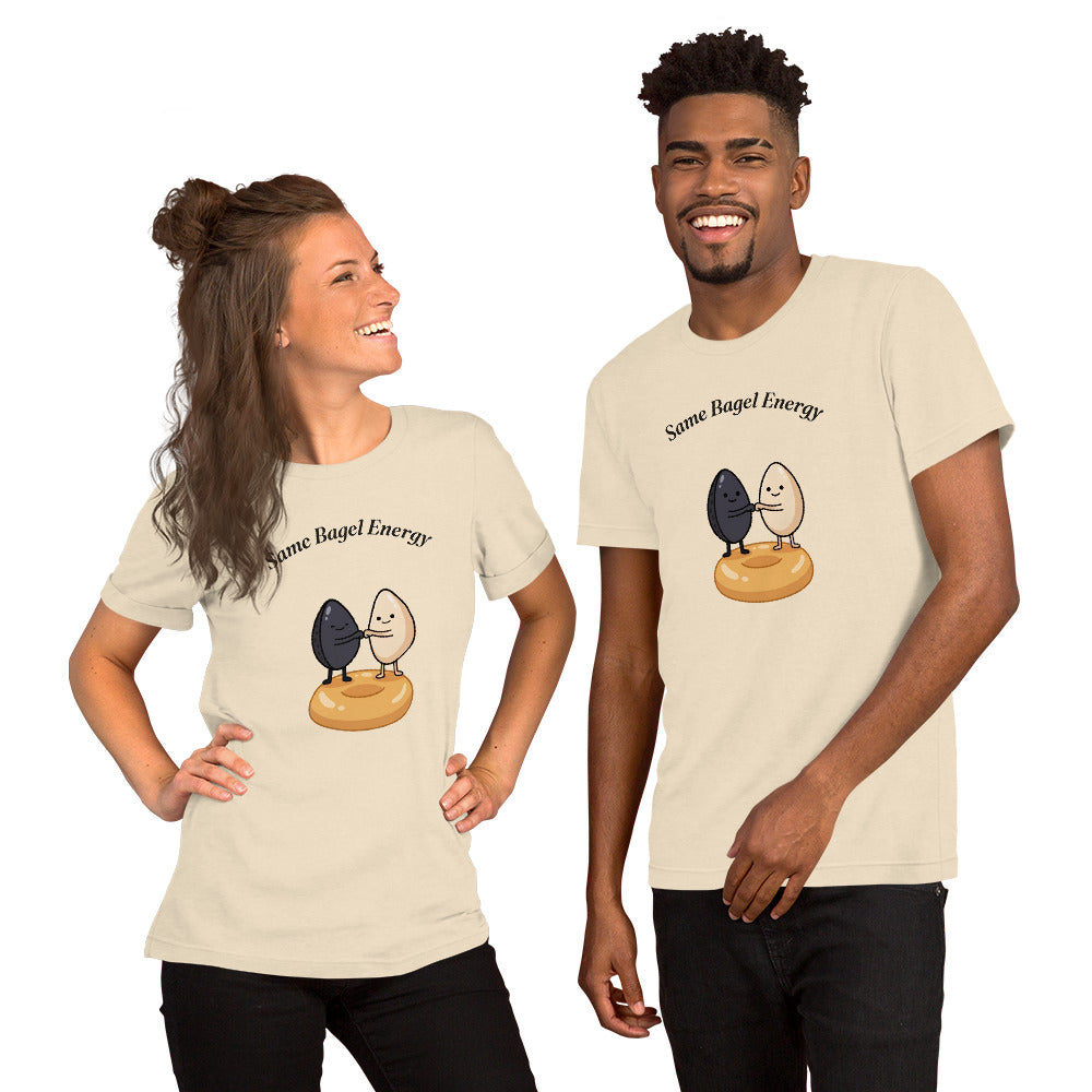 Same Bagel Energy t-shirt with a black sesame seed and a tan sesame seed fist-bumping on a bagel, cream, unisex tee