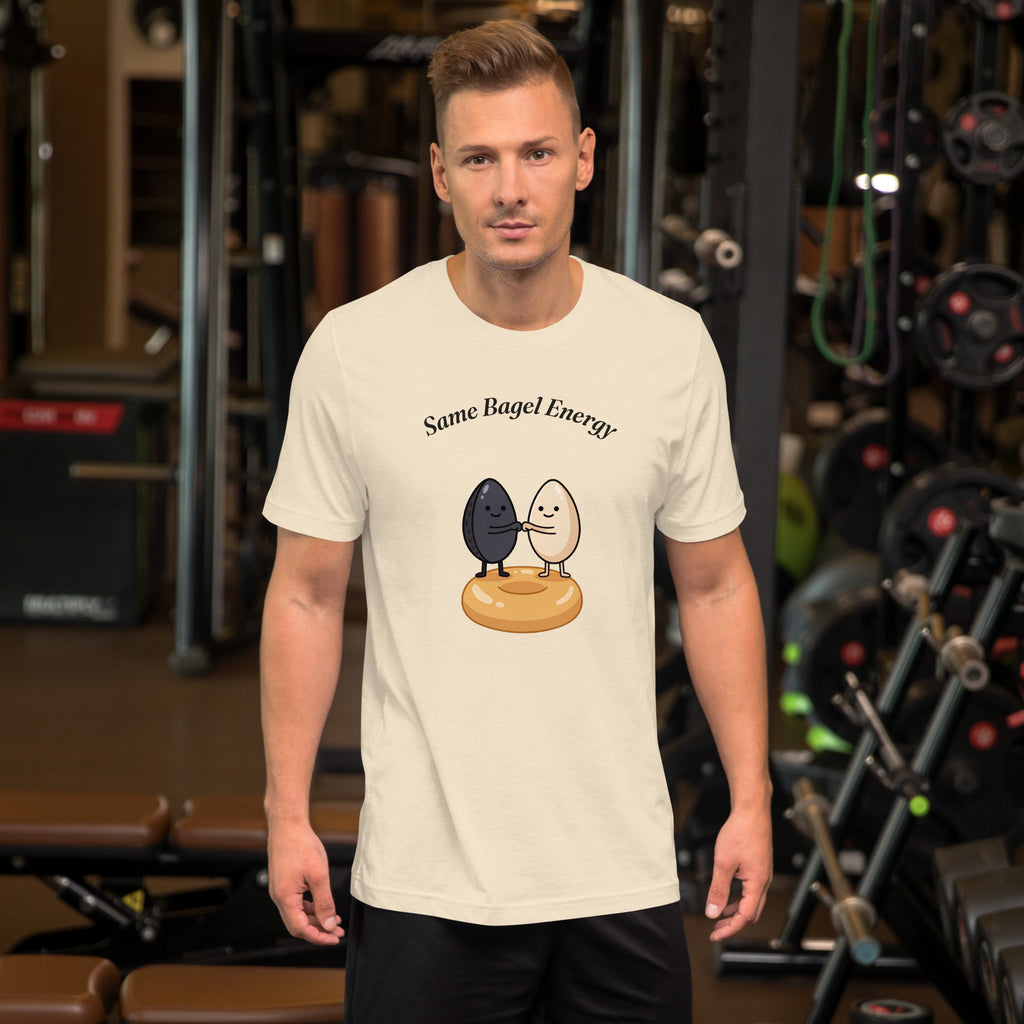 Same Bagel Energy t-shirt with a black sesame seed and a tan sesame seed fist-bumping on a bagel, cream, man