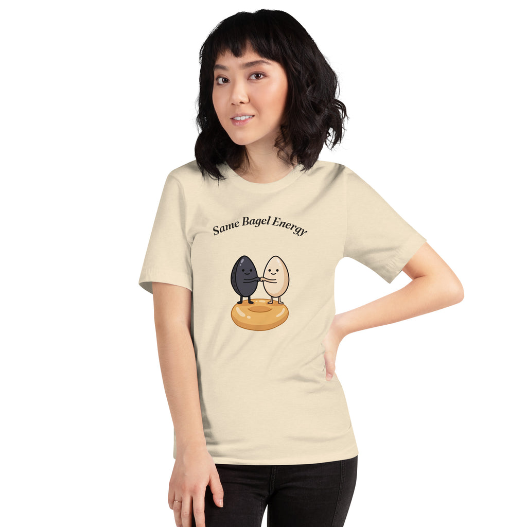 Same Bagel Energy t-shirt with a black sesame seed and a tan sesame seed fist-bumping on a bagel, cream, girl