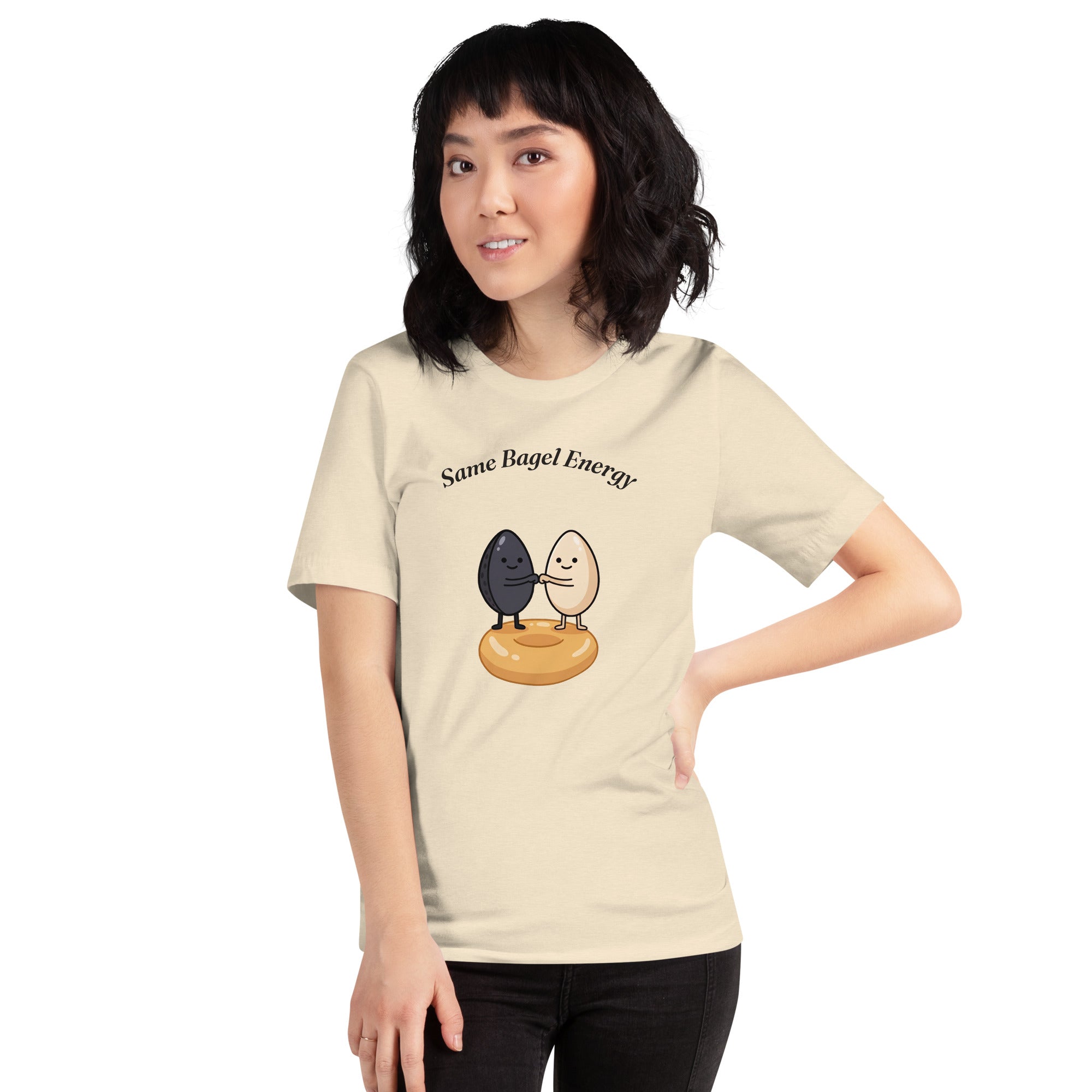 Same Bagel Energy t-shirt with a black sesame seed and a tan sesame seed fist-bumping on a bagel, cream, girl